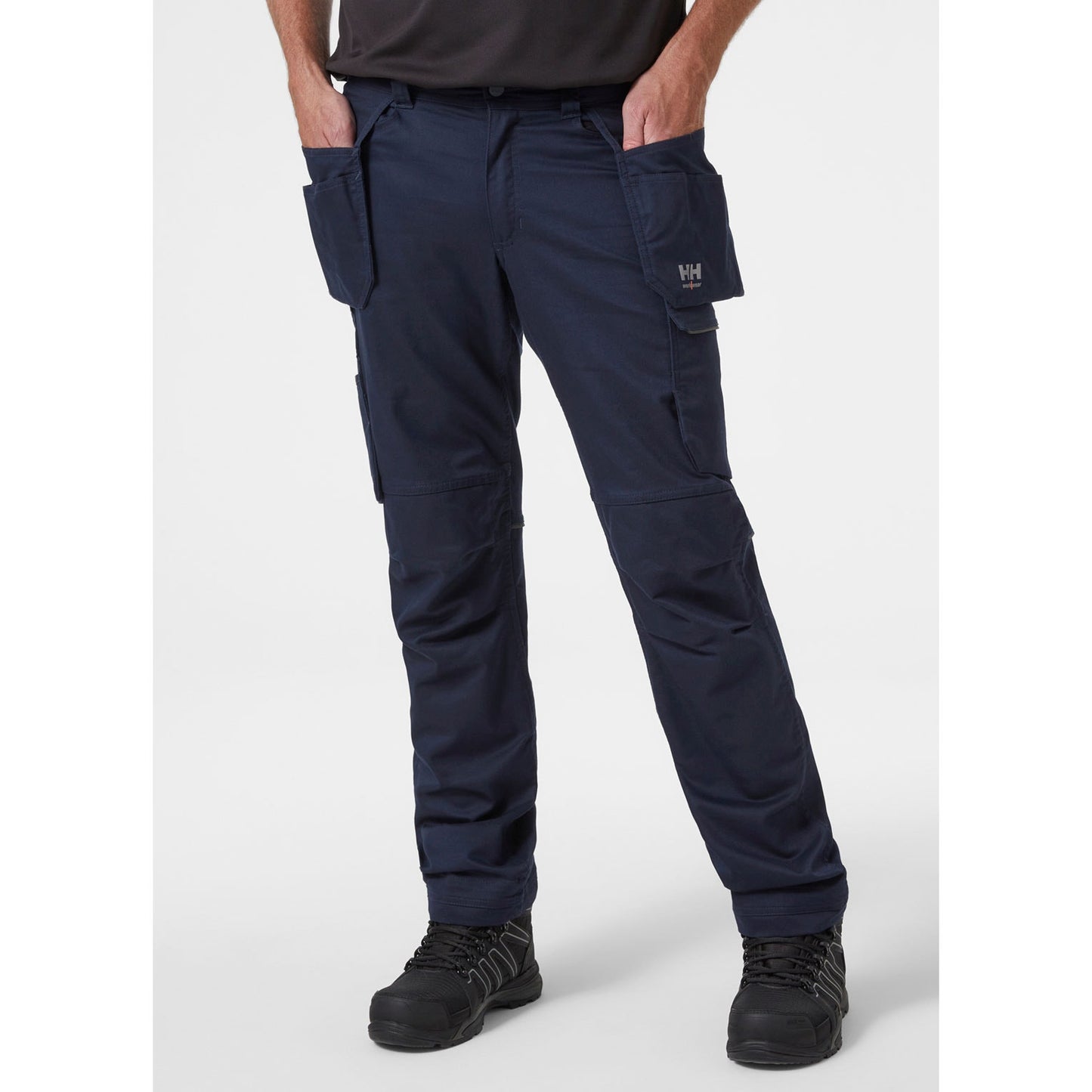 Pogled od spredaj na obrtnika, ki nosi mornarsko modre delovne hlače Helly Hansen Manchester Construction, kar prikazuje kroj in namestitev visečih žepov