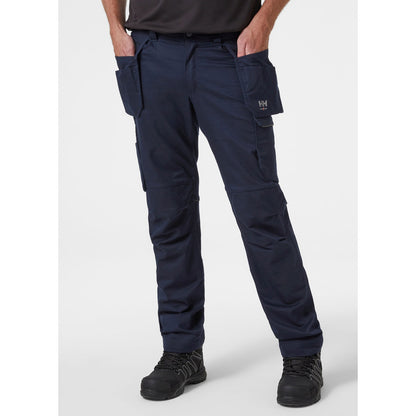 Pogled od spredaj na obrtnika, ki nosi mornarsko modre delovne hlače Helly Hansen Manchester Construction, kar prikazuje kroj in namestitev visečih žepov