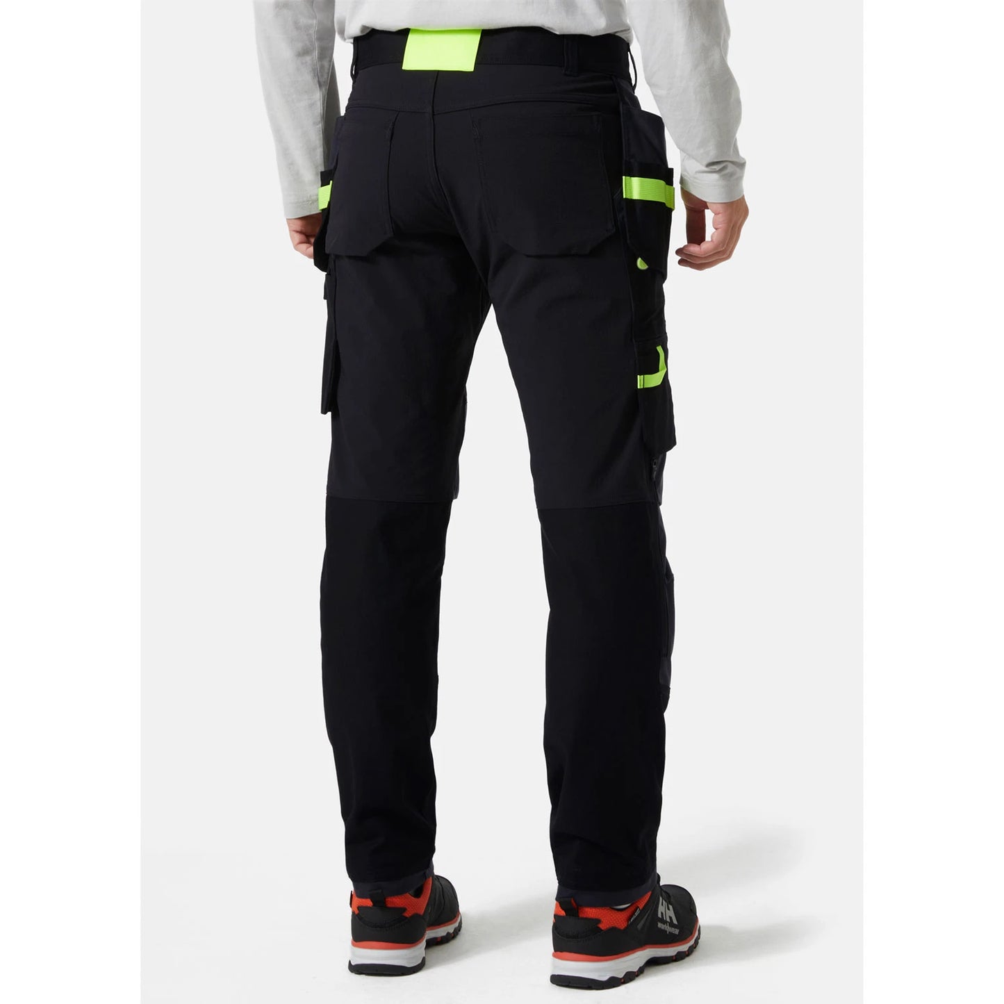 Pogled od zadaj na obrtnika, ki nosi črne premium delovne hlače Helly Hansen Oxford Construction, kar prikazuje kroj in stabilnost zadnjega pasu