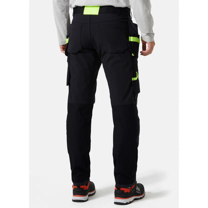 Pogled od zadaj na obrtnika, ki nosi črne premium delovne hlače Helly Hansen Oxford Construction, kar prikazuje kroj in stabilnost zadnjega pasu
